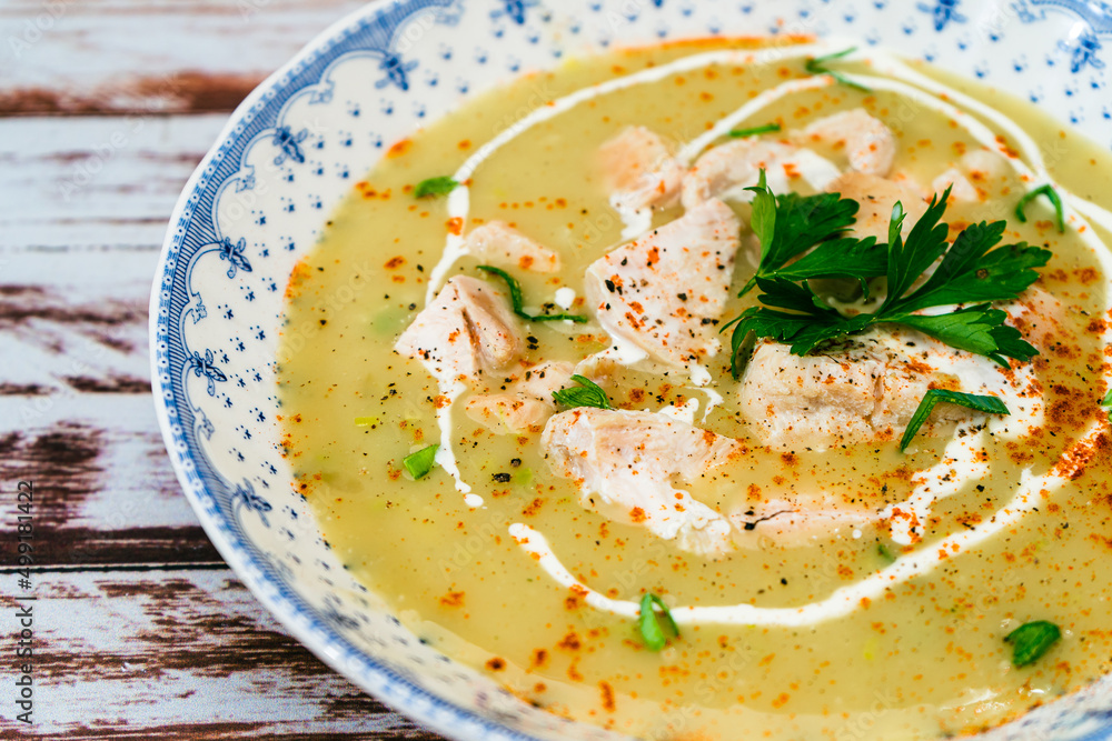 Exquisite dish with a homemade cream of poultry soup with chicken pieces, parsley and cream on a rustic or country style wooden table. Natural and simple food concept. High view Exquisite dish with a homemade cream of poultry soup with chicken pieces, parsley and cream on a rustic or country style wooden table. Natural and simple food concept. High view