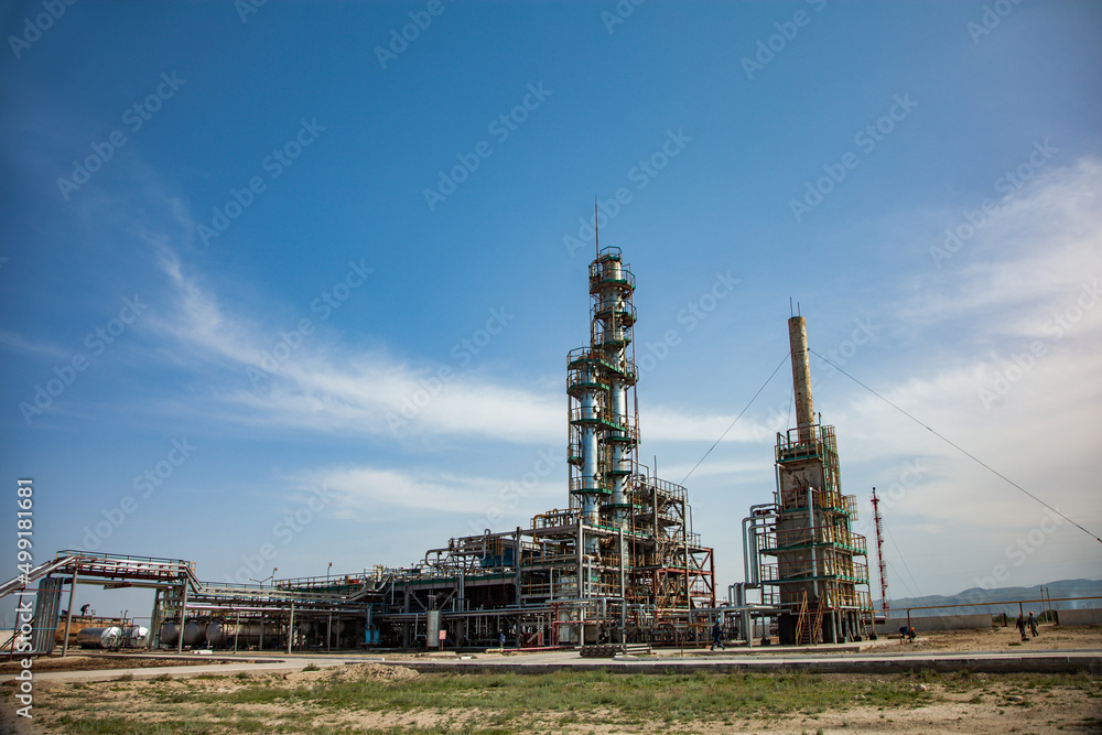 Grey distillation tower (refinery column) on blue sky with clouds and mountains. Oil refinery plant in desert near Taraz city, Kazakhstan.