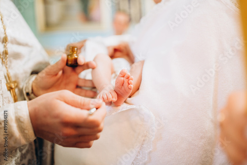 Baptism ceremony of a baby. Close up of tiny baby feet  the sacrament of baptism. The godfather holds the child in his arms. small legs of a newborn baby