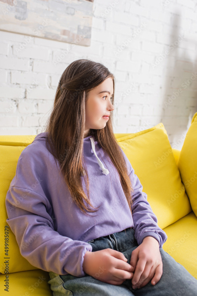 Side view of teen girl with down syndrome sitting on couch at home. Side view of teen girl with down syndrome sitting on couch at home.