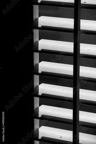 wooden window shutters or blinds open letting light in through window geometrical shapes and pattern of rectangles squares and lines of shadows and light 