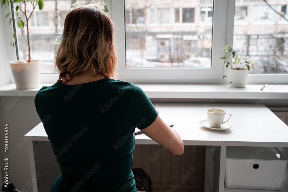 Young woman sitting at the table by the window and writing. Young woman sitting at the table by the window and writing.