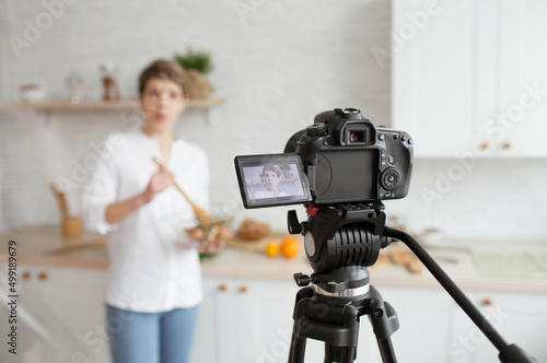 A young pretty blogger girl is recording a video tutorial on cooking salads in a home kitchen.