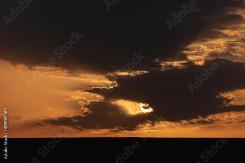 The sun in the sky with dark, thick clouds at sunset.