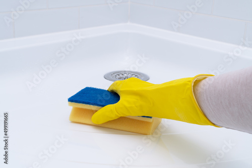 Hand in rubber glove cleaning acrylic shower tray.