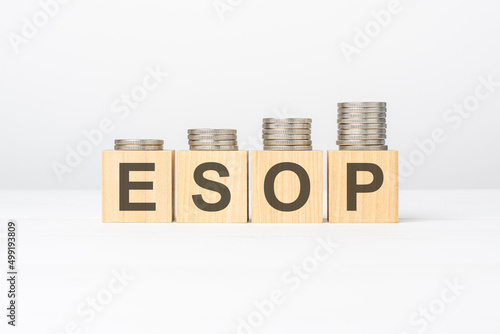 esop text written on wooden block with stacked coins on white background photo