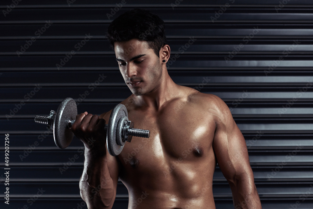 Building his body. Cropped shot of an athletic young man working out with a dumbbell.