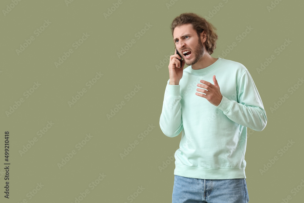 Angry young man talking by mobile phone on green background Angry young man talking by mobile phone on green background
