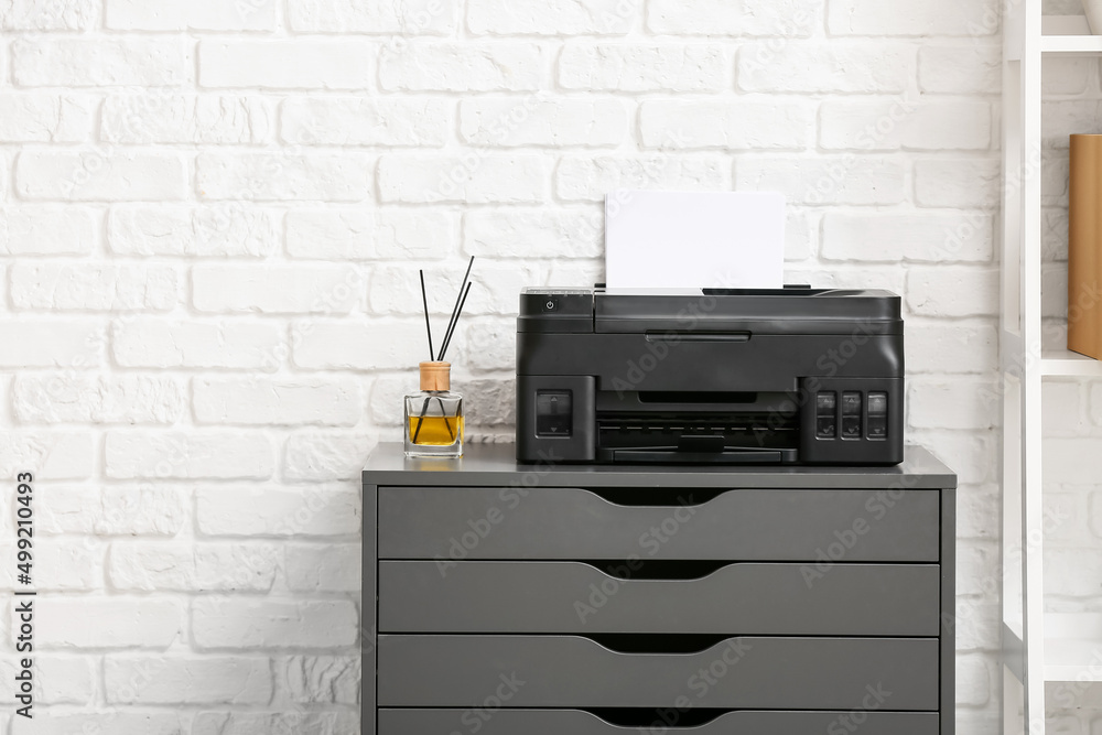 Chest of drawers with modern printer and reed diffuser near white brick wall Chest of drawers with modern printer and reed diffuser near white brick wall