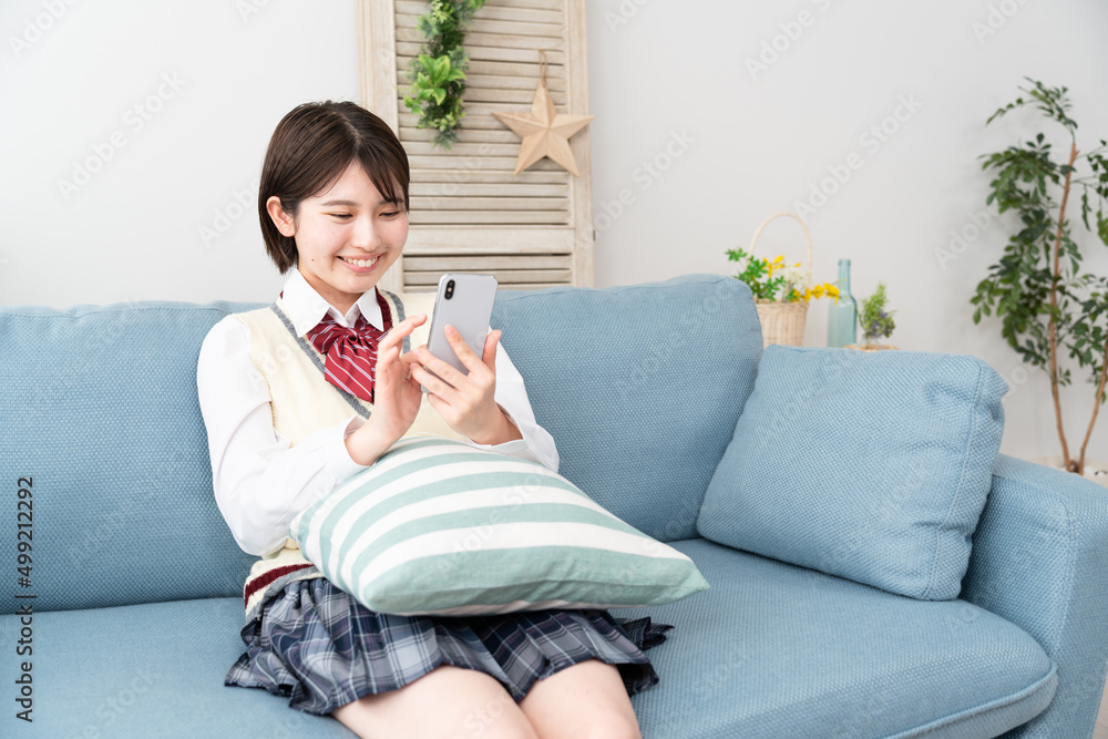 ソファーでスマートフォンを操作する女子高生 ソファーでスマートフォンを操作する女子高生