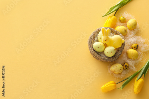 Nest with painted Easter eggs, tulip flowers and bunny on yellow background