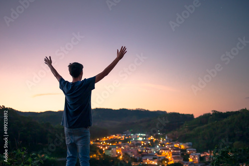 Man with arms raised thanking and worshiping God  under the dusk sky and with city lights in the background. Concept of faith  religion or spirituality.