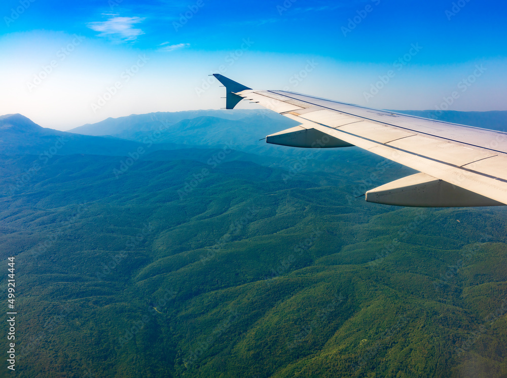 View of airplane wing, blue skies and green land during landing. Airplane window view. View of airplane wing, blue skies and green land during landing. Airplane window view.