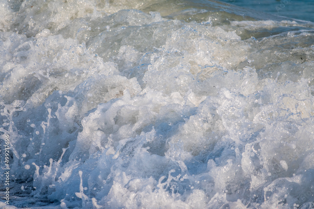 Splashes of water and foam against the sea on a sunny summer day