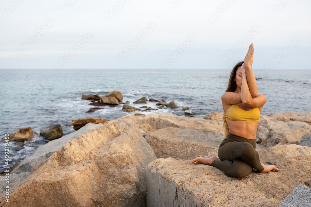 Young woman doing gomukhasana with garudasana arms. Yoga practice in nature near the ocean.Copy space. Young woman doing gomukhasana with garudasana arms. Yoga practice in nature near the ocean.Copy space.
