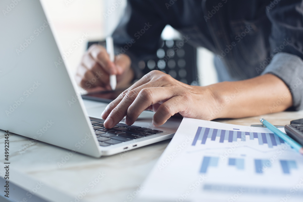 Business man working at office with laptop computer and digital tablet and financial report graph data documents on his desk, close up Business man working at office with laptop computer and digital tablet and financial report graph data documents on his desk, close up