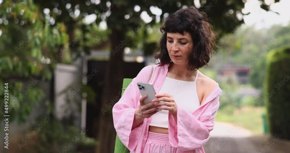 Modern young caucasian woman is using smartphone video chatting walking outdoors. Brunette wears casual pink clothes in summer. technology concept Modern young caucasian woman is using smartphone video chatting walking outdoors. Brunette wears casual pink clothes in summer. technology concept