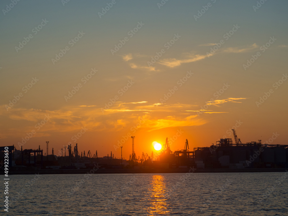 Beautiful sunset above port on sunset time with silhouettes of cargo cranes. Industrial black sea port Odesa, Ukraine with a lot of cranes, cabins, boxes and tanks by the water on colorful sunset