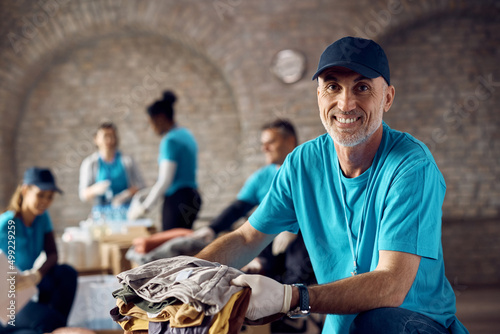 Happy mature volunteer packing clothes in donation boxes and looking at camera.
