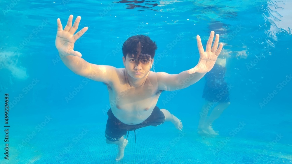 Portrait of asian boy underwater in swimming pool with glass wall. Happy handsome boy in mask dive and swim underwater