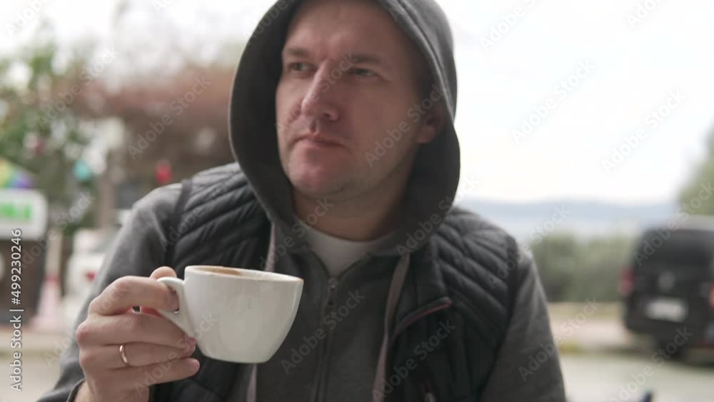 A brutal man drinks coffee at a table in a cafe on the street, close-up. A brutal man drinks coffee at a table in a cafe on the street, close-up.