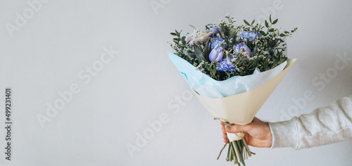 Young man in grey with bouqet of flowers in hands on grey background, banner photo