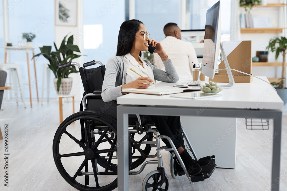 Shes always on call and available. Full length shot of an attractive young businesswoman in a wheelchair making a phonecall while working at her desk in the office. Shes always on call and available. Full length shot of an attractive young businesswoman in a wheelchair making a phonecall while working at her desk in the office.