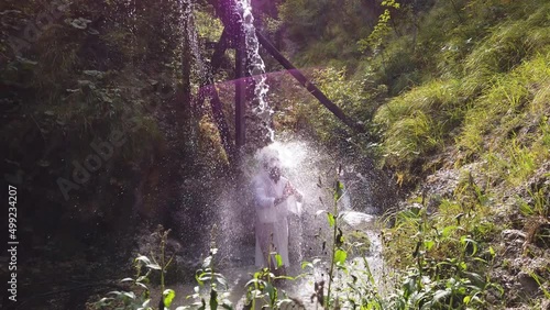 european buddhist shugendo monk standing under waterfall with white robe and meditating