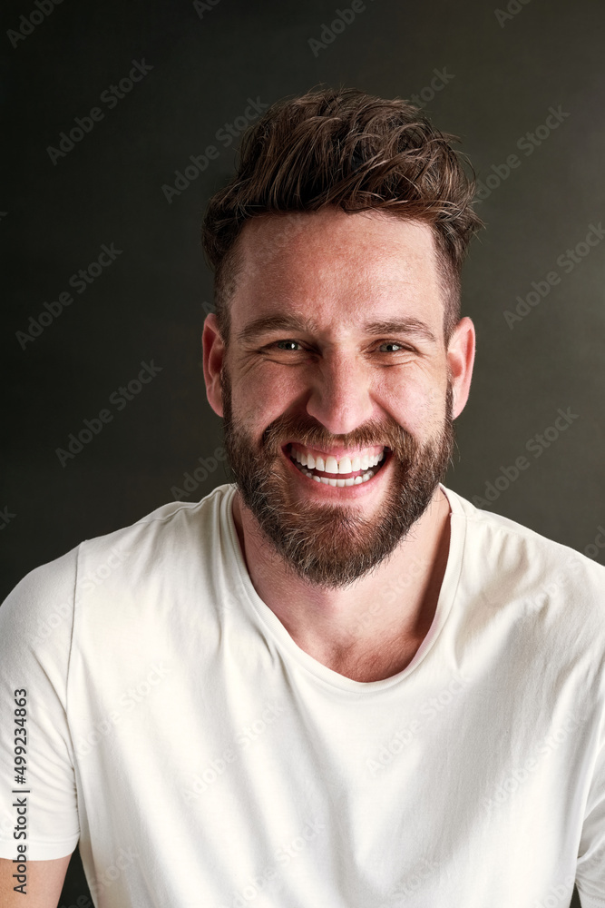 Smile, and the whole world smiles with you. Portrait of a happy young man posing against a dark background in studio. Smile, and the whole world smiles with you. Portrait of a happy young man posing against a dark background in studio.
