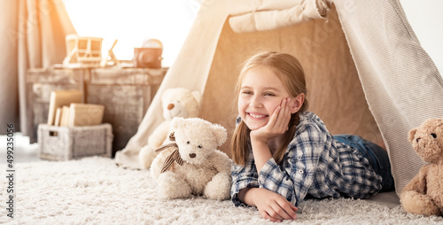 Little girl lying in wigwam with plush teddies in light room
