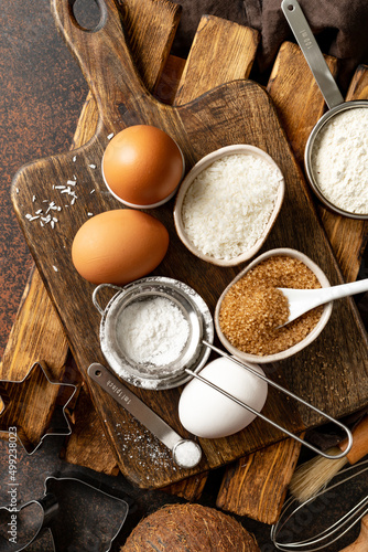 Ingredients for coconut cookies or sweet pastries on a culinary background. Eggs, coconut chips, flour, sugar and salt on a dark table. Top view	