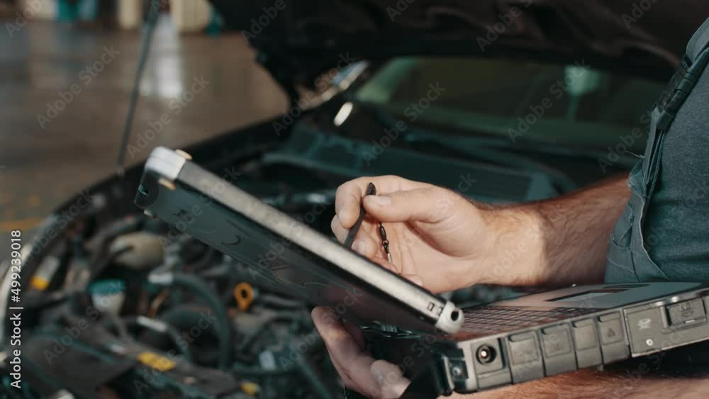 Auto service, maintenance concept. Close up of hands car electrician repairs car. Mechanic use notebook computers to record engine checks collect detailed information during work Auto service, maintenance concept. Close up of hands car electrician repairs car. Mechanic use notebook computers to record engine checks collect detailed information during work