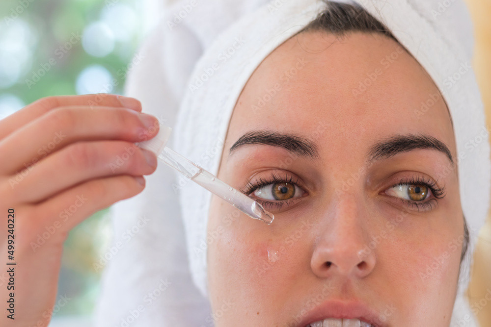 Beautiful woman applying hyaluronic acid on her face with a towel rolled up