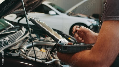 Hands of mechanic working in auto repair shop. Car electrician repairs car. Mechanic use notebook computers to record engine checks collect detailed information during work