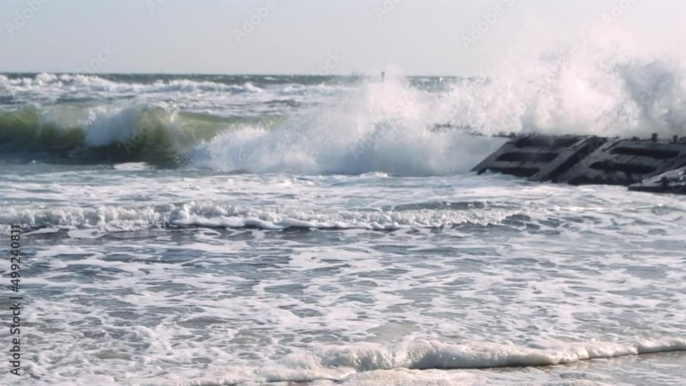 Strong high sea waves break on stone with concrete slab breakwater old pier. Stormy sea. Waves of stormy sea roll on sandy shore on sunny day. Seacoast, seashore, seaside. Natural background Strong high sea waves break on stone with concrete slab breakwater old pier. Stormy sea. Waves of stormy sea roll on sandy shore on sunny day. Seacoast, seashore, seaside. Natural background
