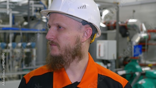 Close-up of the face of an engineer in a white helmet with a beard in the building of an industrial production workshop for pumping oil and gas condensate. Petrochemical industry