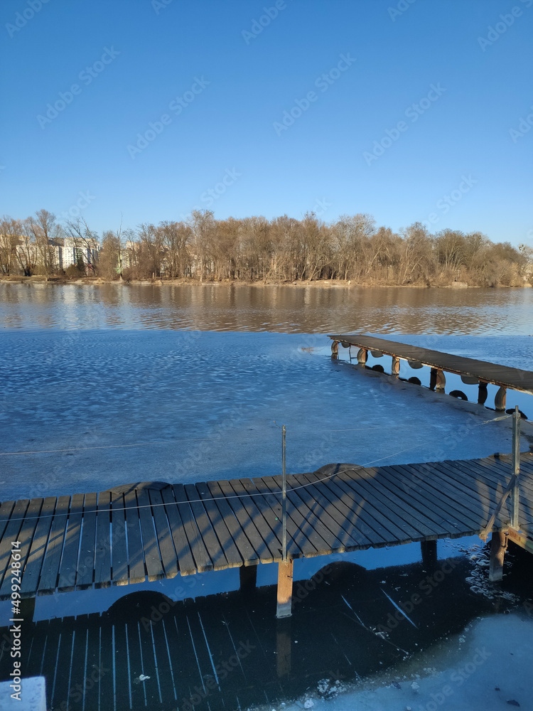Naklejka premium wooden pier on a river covered with ice in winter