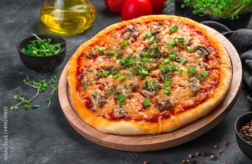 Pizza with cheese, mushrooms, tomatoes and herbs on a wooden board on a dark background.