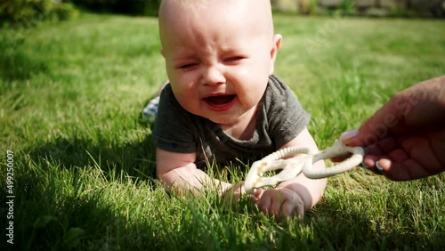 two-month-old baby lies on lawn and cries, mom's hand gives a toy
