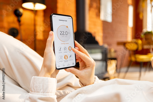 Woman holding phone with running smart home application for heating temperature control, while lying relaxed at home. Close-up on device screen photo