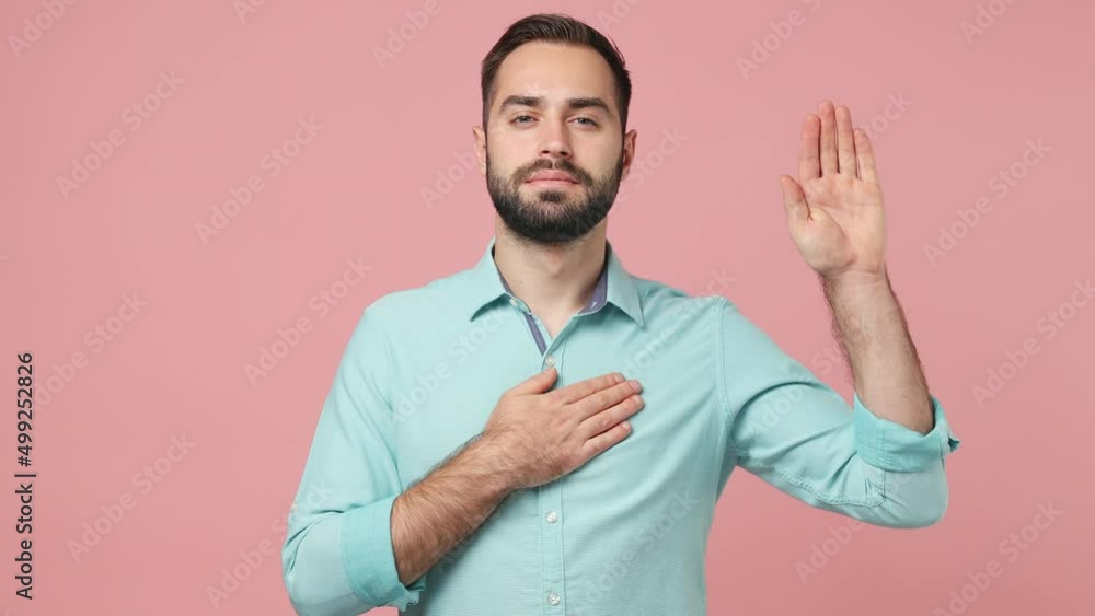 Serious swanky young brunet man 20s years old wears blue shirt looking camera raise put hand on chest swear promise isolated on plain plain pink background studio. People emotions lifestyle concept Serious swanky young brunet man 20s years old wears blue shirt looking camera raise put hand on chest swear promise isolated on plain plain pink background studio. People emotions lifestyle concept
