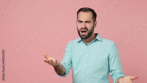 Side profile view shocked young brunet man 20s wears blue shirt looking camera spreading hands ask what why wave hand isolated on plain plain pink background studio. People emotions lifestyle concept