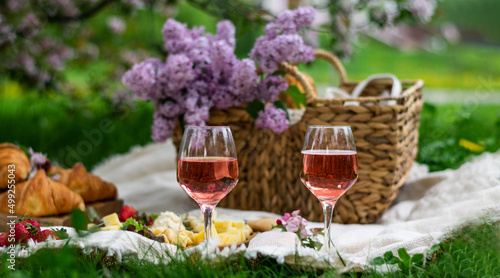 Closeup of two glass of rose wine , picnic basket, croissants, food and flowers on the grass. Banner