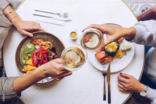 Friends holding a glass of wine and toasting. Top view of brunch table.