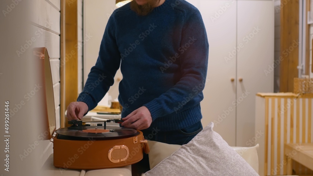 A man puts a record in a gramophone to listen to classical music. A vinyl record of classical music is used in a gramophone player. Put on a record to listen to music