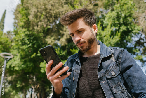 Side view portrait of a sad man in a lonely city park using a smart phone. Man reading a message or checking phone messages or watching video