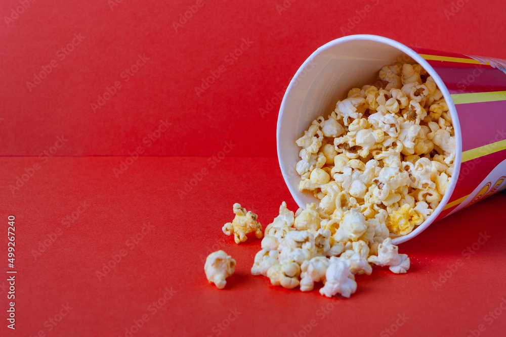 popcorn spills out of a striped paper bucket on a red background, copy space popcorn spills out of a striped paper bucket on a red background, copy space