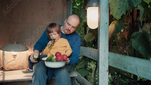 Father and a small child eat fresh, organic vegetables from a farm sitting on the porch of a country farm. The concept of healthy bio organic food and natural products without pistecides and nitrates