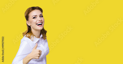 Excited happy smiling businesswoman, showing thumb finger up or like hand sign gesture. Success in business studio concept. Isolated over yellow color background. photo