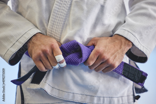 Hes a seasoned professional. Cropped shot of an unrecognizable man tying a purple belt around hist waist while in full jiu jitsu gi. photo